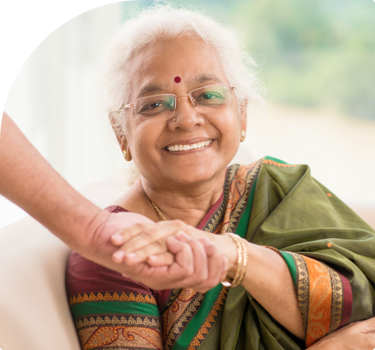 An elder smiling at ease at home, holding hands with a family member.